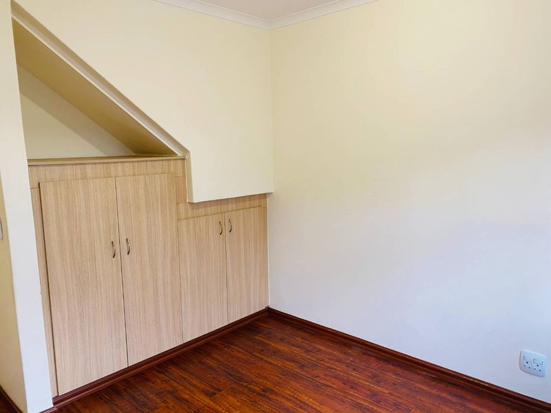 A clean, empty bedroom featuring light wood-toned built-in cabinetry, dark laminate flooring, and neutral wall finishes, offering a versatile space for various uses.