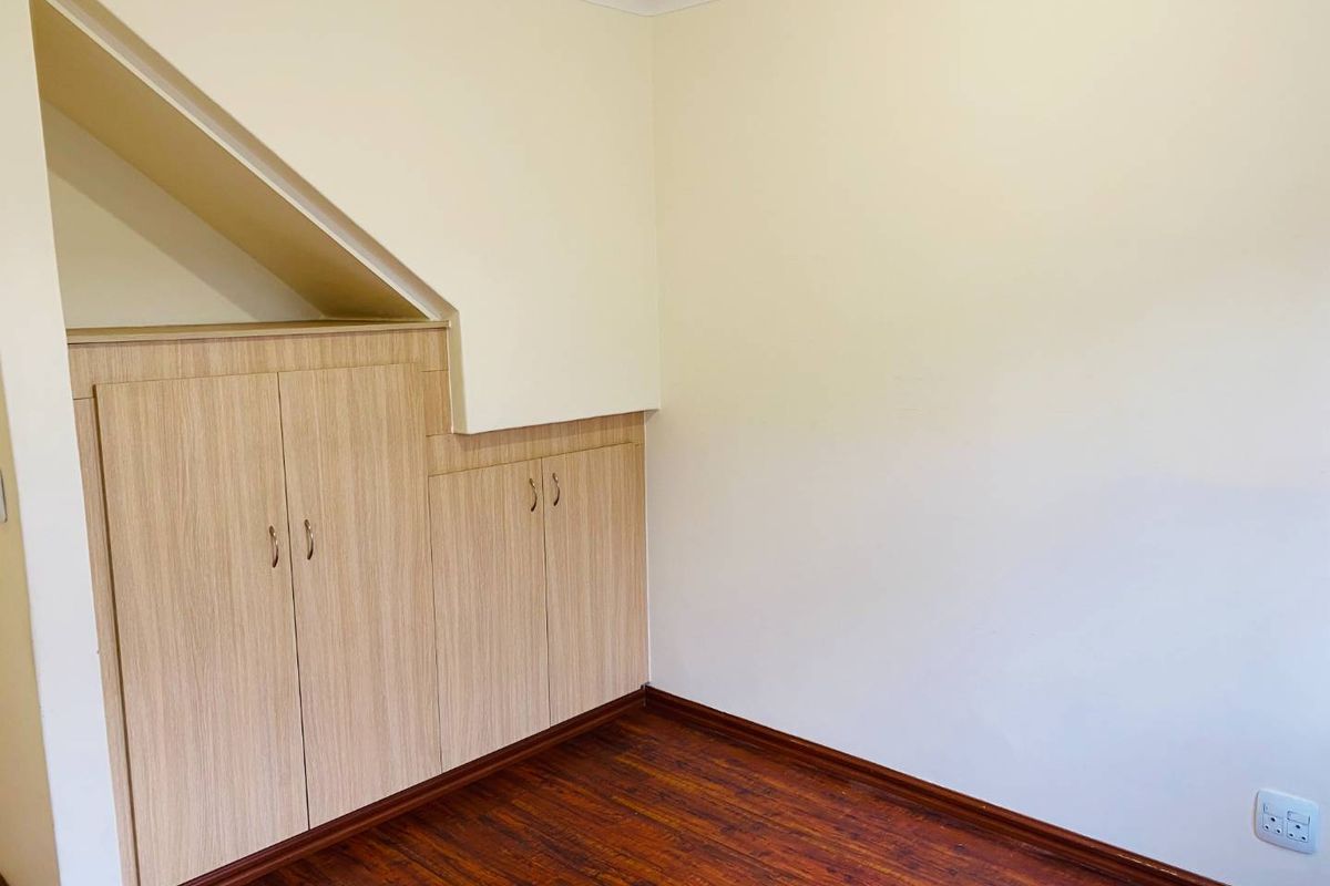 A clean, empty bedroom featuring light wood-toned built-in cabinetry, dark laminate flooring, and neutral wall finishes, offering a versatile space for various uses.