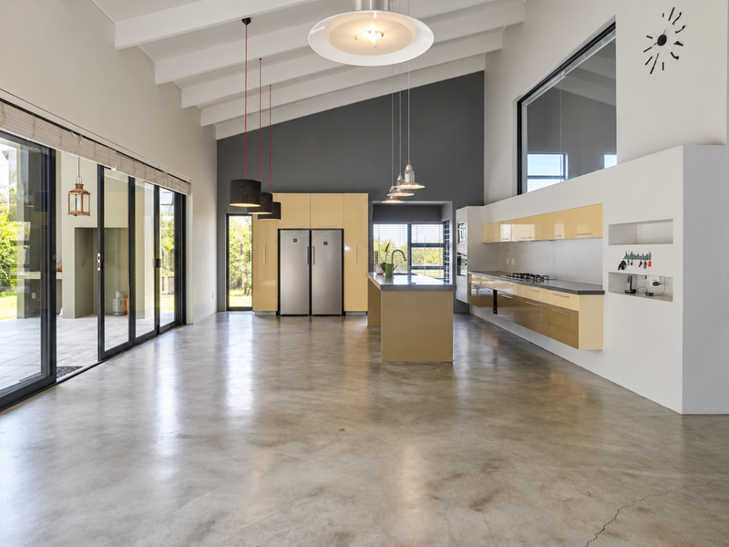 Spacious open-plan kitchen and living area featuring polished concrete floors, vaulted ceilings with exposed beams, and modern built-in cabinetry with a central island.