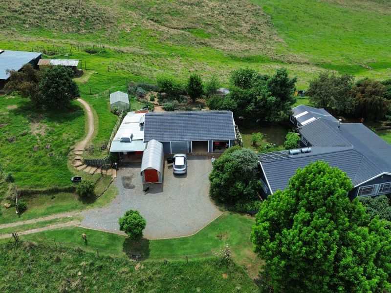 Aerial view of a small holding property featuring multiple buildings with tiled roofs, solar panels, and a gravel driveway set within a rural landscape.