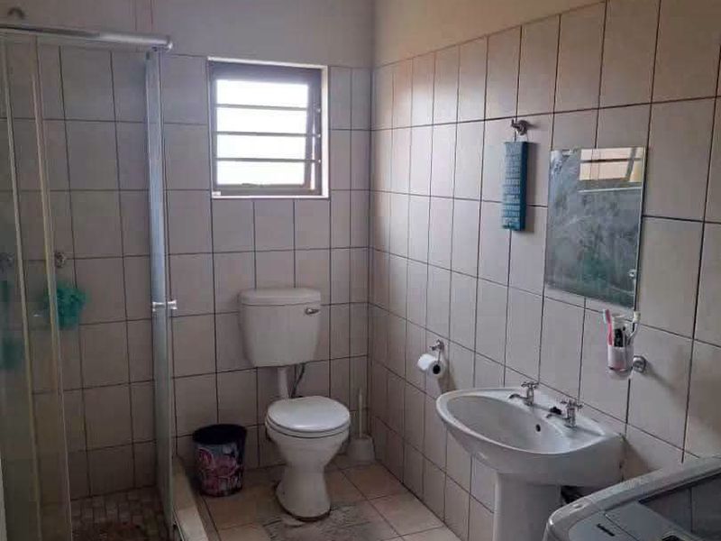 A functional bathroom featuring a shower enclosure, pedestal basin, and toilet with neutral wall and floor tiling.
