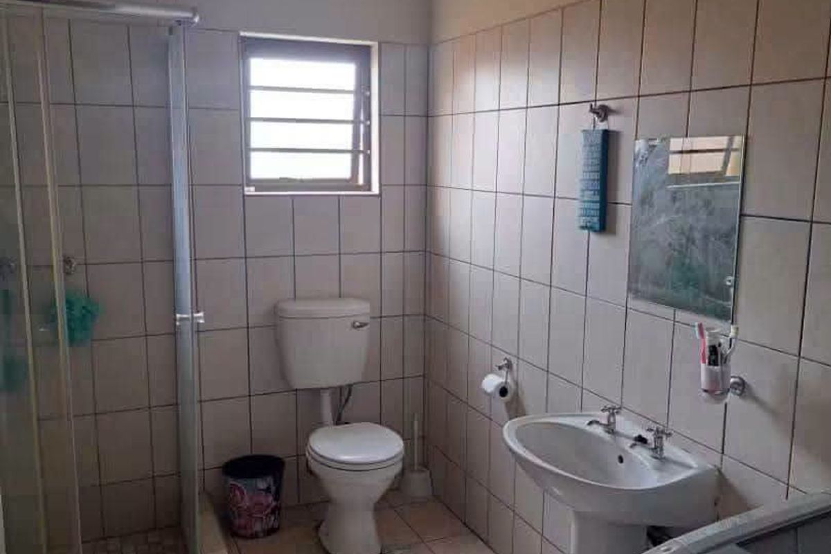 A functional bathroom featuring a shower enclosure, pedestal basin, and toilet with neutral wall and floor tiling.