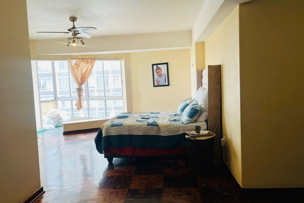 Spacious bedroom featuring classic parquet flooring, a ceiling fan, and large windows that provide ample natural light.