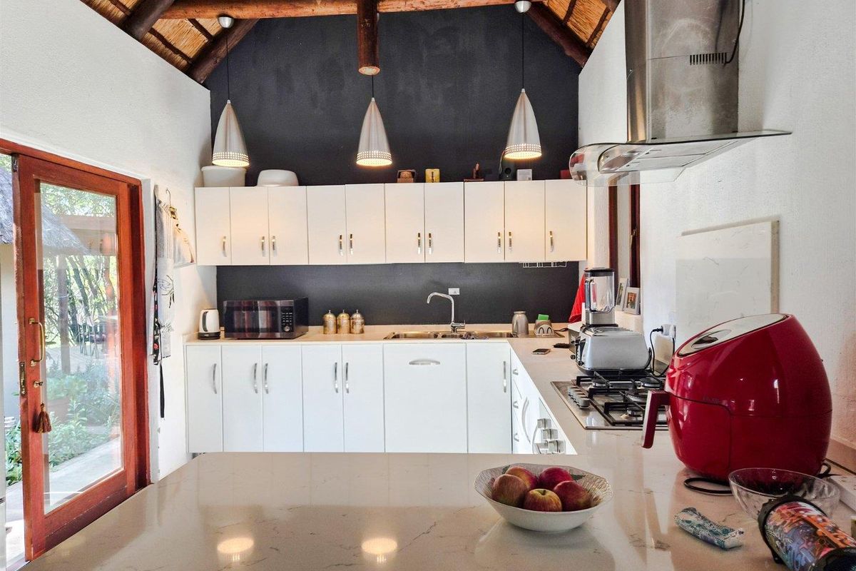 A well-lit kitchen featuring white cabinetry, stone countertops, a gas hob with extractor fan, and a high vaulted thatched ceiling.