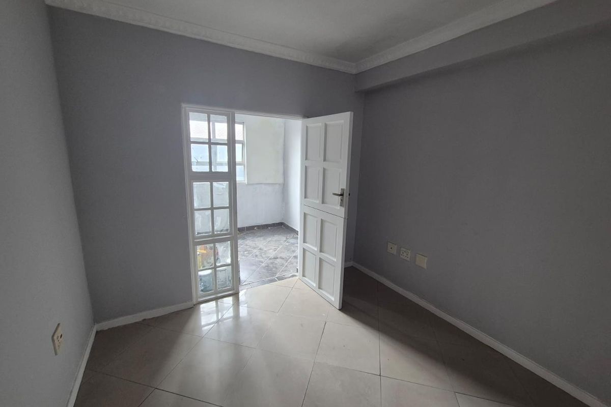 An empty bedroom featuring tiled flooring, decorative cornice, and a door leading to an adjacent balcony area.