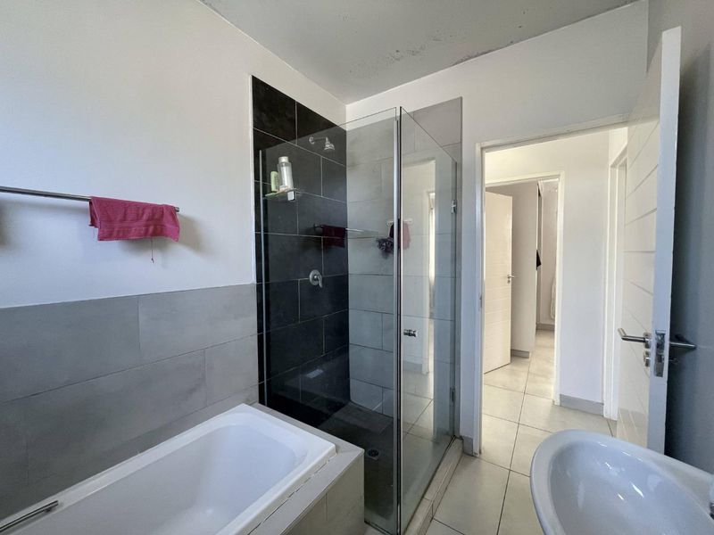 A functional bathroom featuring a built-in bathtub, a separate glass-enclosed shower, and tiled finishes, requiring minor ceiling maintenance.