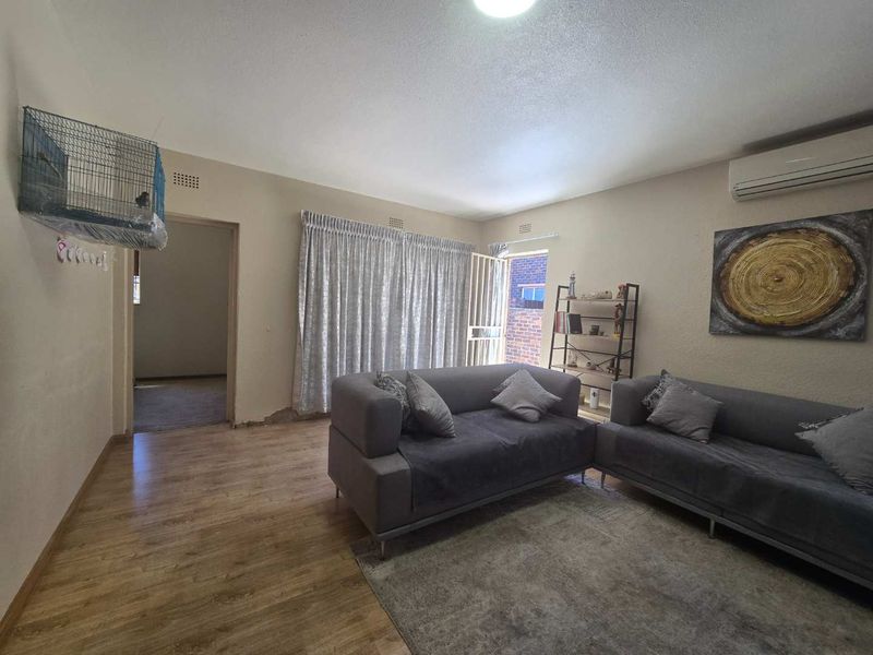 A living room featuring laminate flooring, an air conditioning unit, and a security gate leading to the exterior.