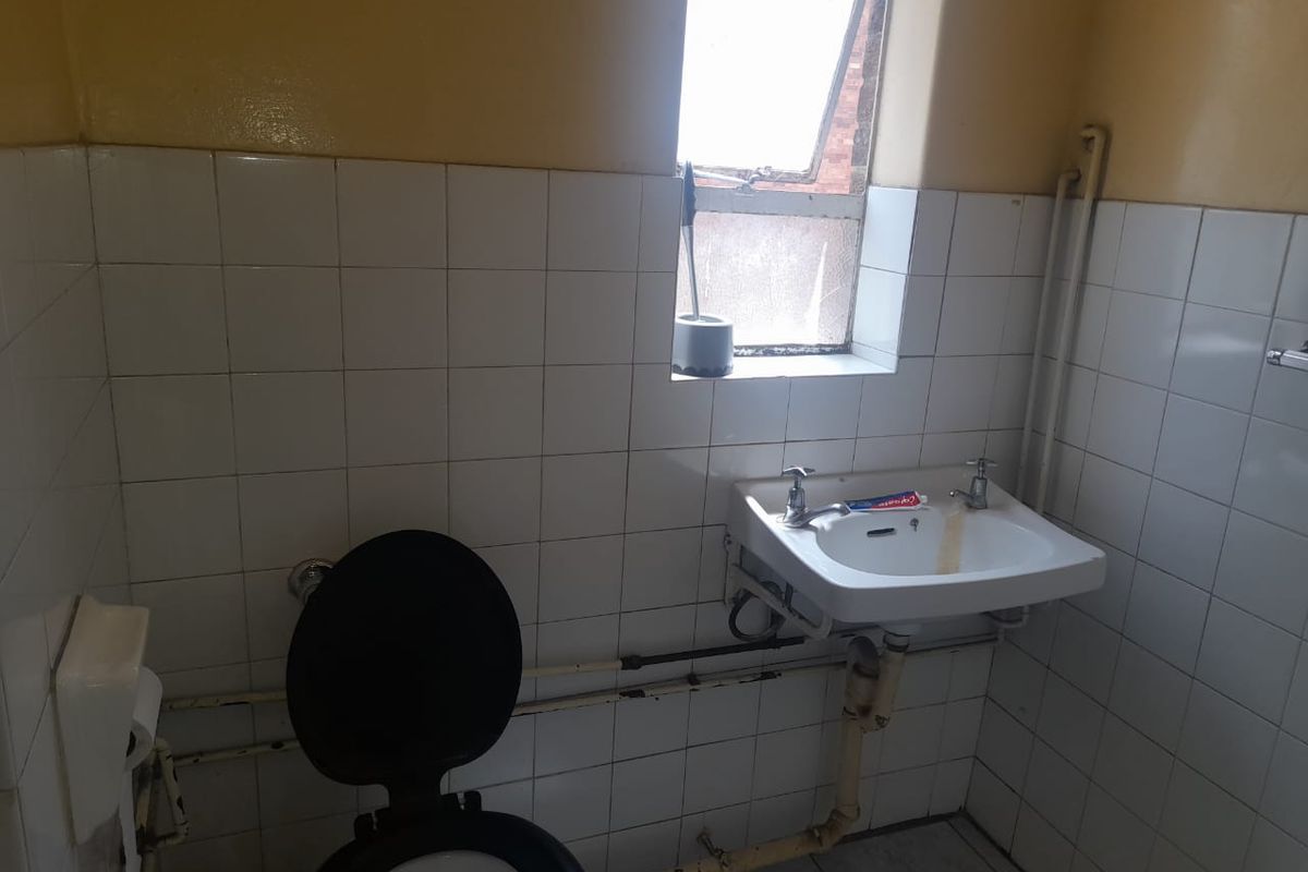 A compact bathroom featuring a wall-mounted basin, toilet, and tiled walls with exposed plumbing fixtures.