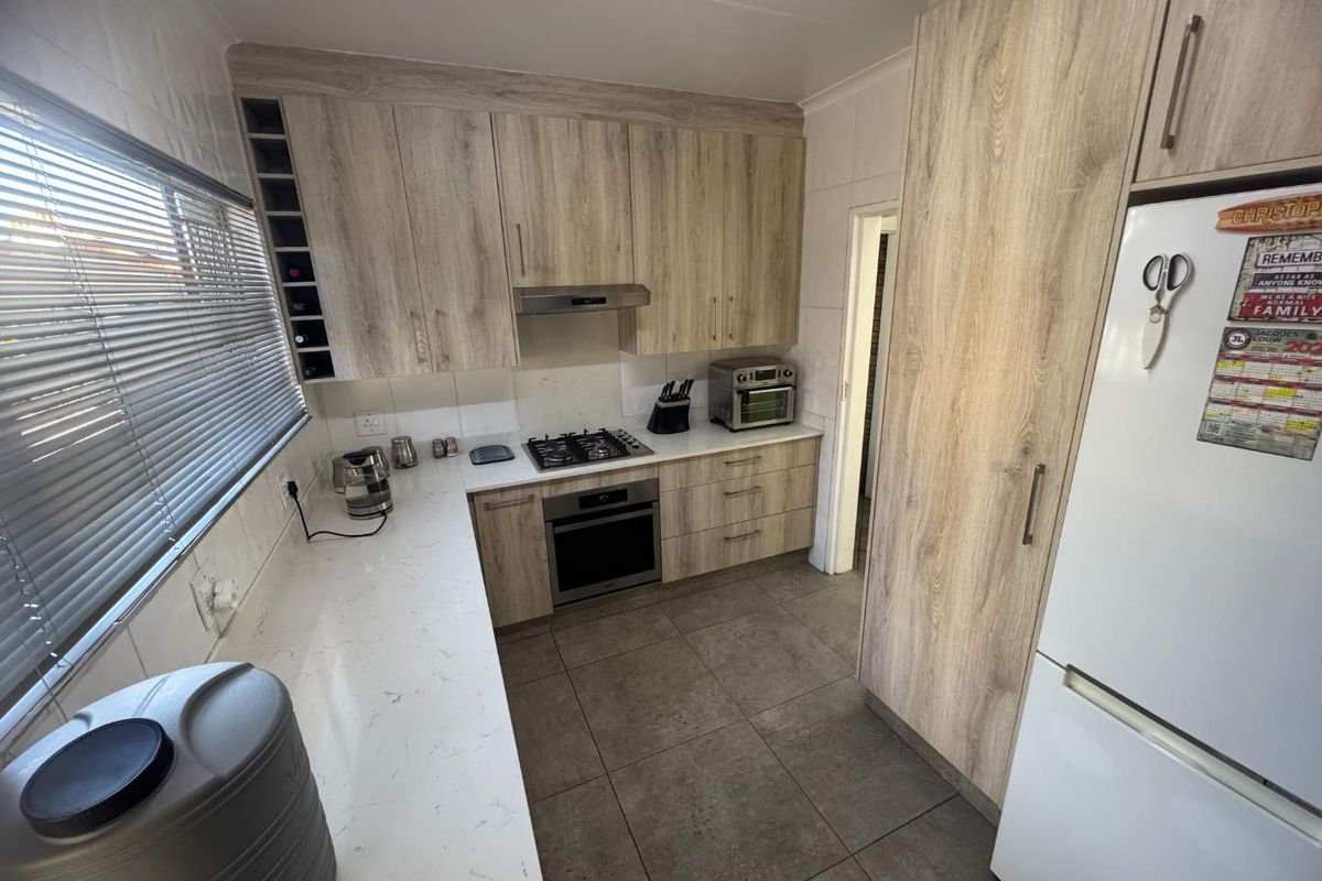 Modern kitchen featuring light wood-grain cabinetry, stone countertops, built-in oven, gas hob, extractor fan, and tiled flooring.