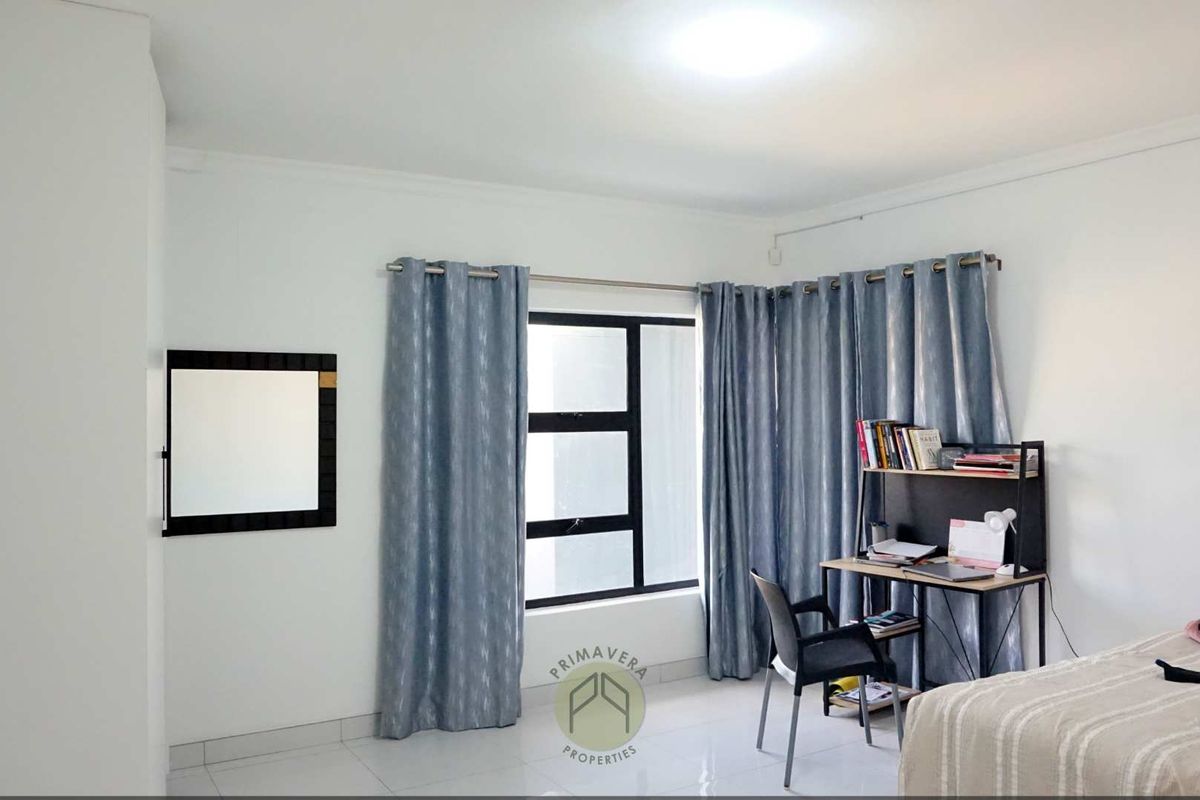 A bright bedroom featuring tiled flooring, large windows with curtain rods, and neutral wall finishes.
