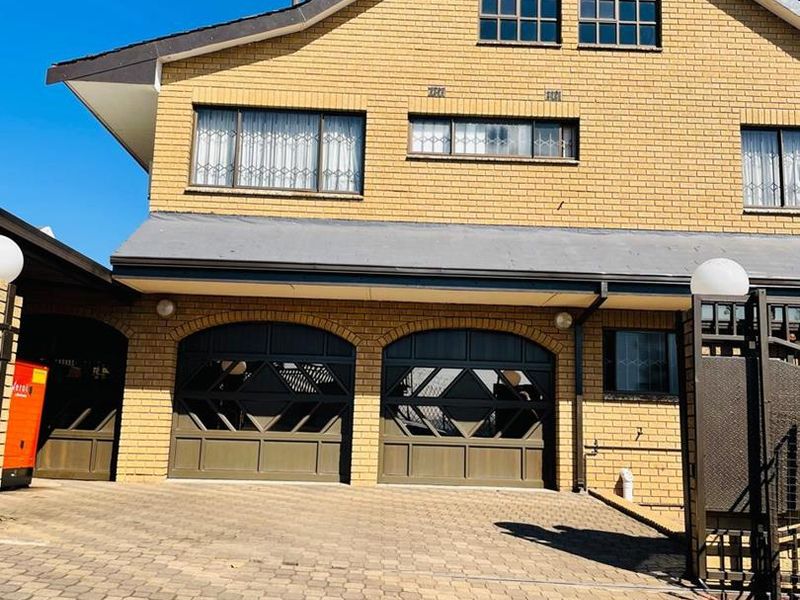 Front elevation of a double-story brick house featuring a paved driveway, double garage, and secure gated entrance.