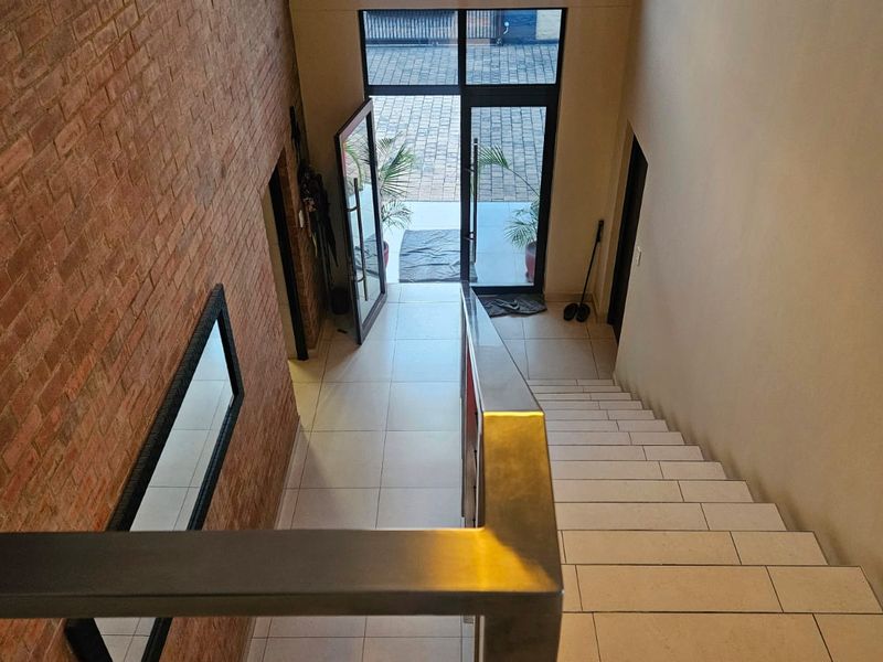 Spacious entrance hall featuring an exposed brick feature wall, modern tiled staircase with stainless steel handrail, and glass door access to the exterior.