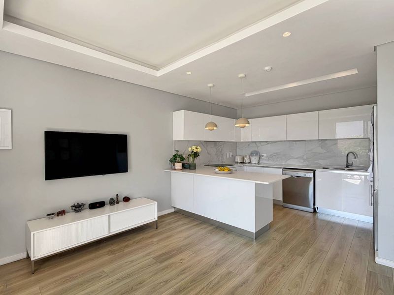 Modern open-plan kitchen and living area featuring sleek white cabinetry, stone countertops, marble-look splashback, and high-quality laminate wood flooring.