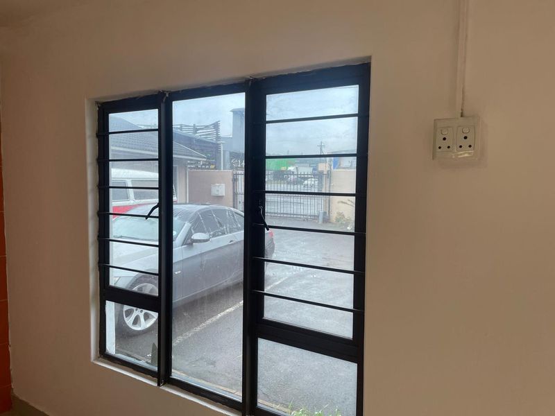 Interior view of a room featuring a large window with black metal security bars and a surface-mounted electrical outlet.