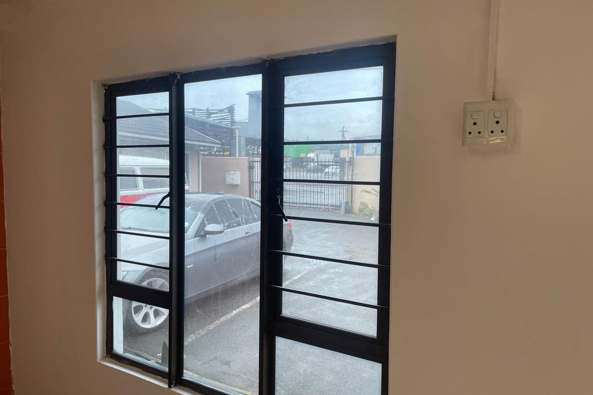Interior view of a room featuring a large window with black metal security bars and a surface-mounted electrical outlet.