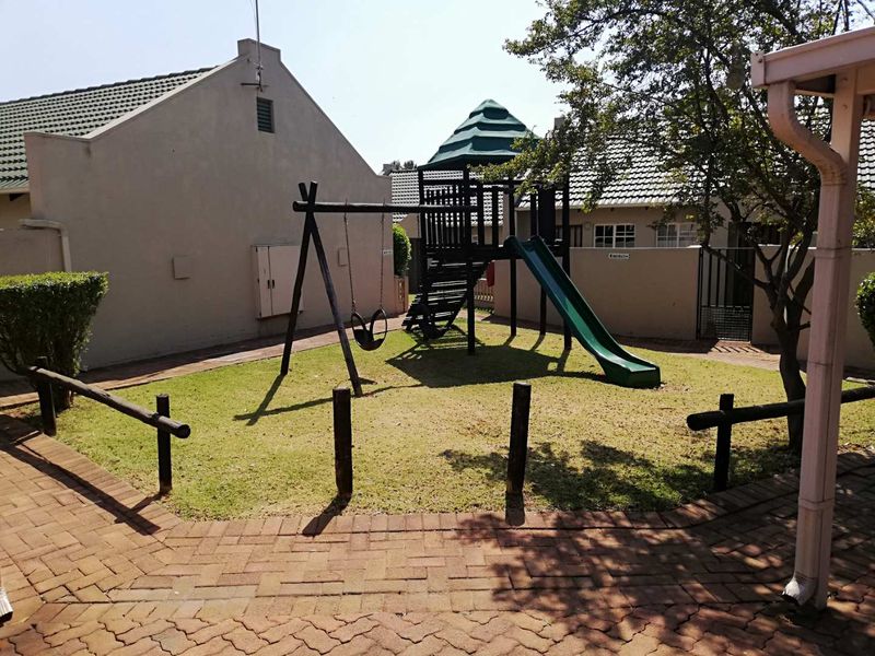 A communal garden area featuring a paved walkway, lawn, and timber post fencing, situated between townhouse units.
