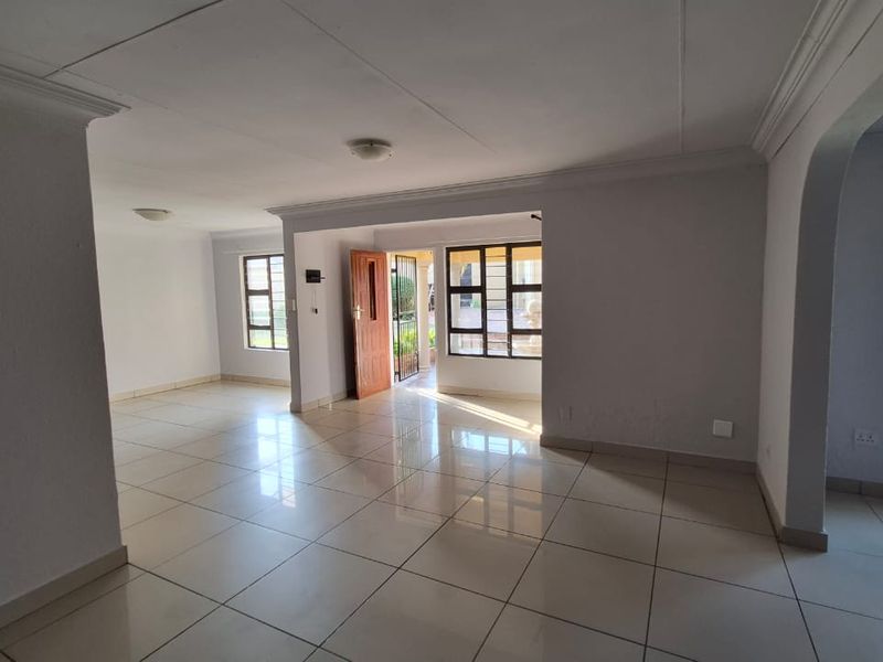 A spacious, empty living area featuring neutral tiled flooring, coved ceilings, and large aluminium-framed windows that provide ample natural light.
