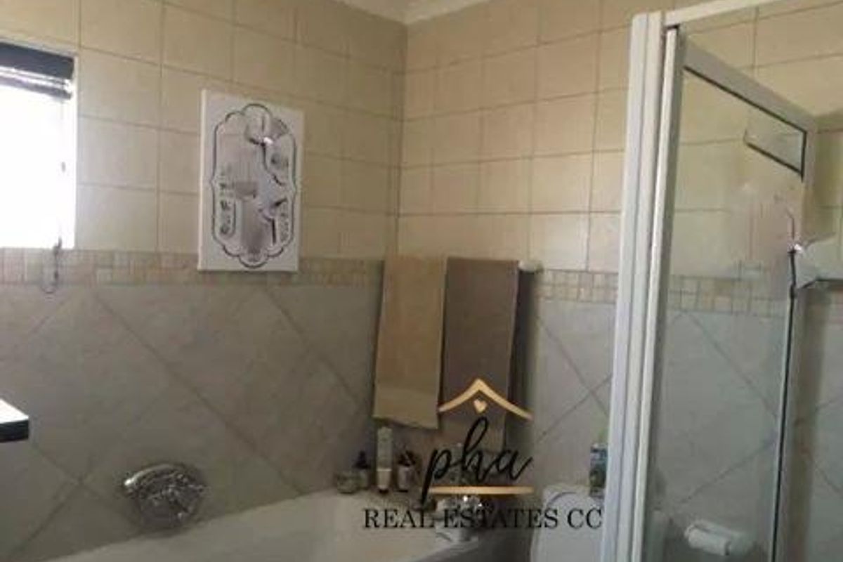 A functional bathroom featuring a built-in bathtub, shower enclosure, and neutral wall tiling throughout.