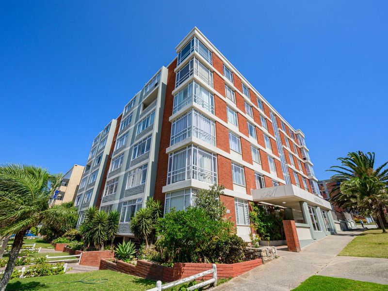 Exterior view of a multi-story apartment building featuring a brick facade, large windows, and a covered entrance area with surrounding landscaped grounds.