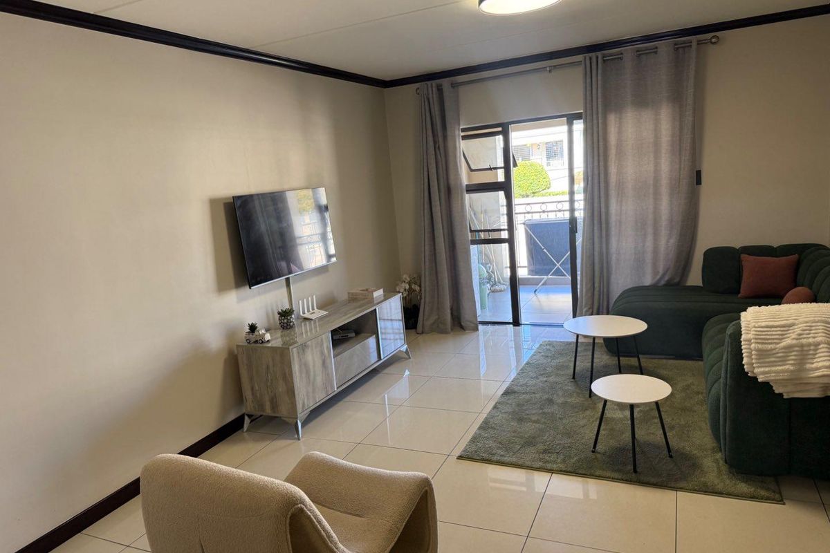 A well-maintained living room featuring large format floor tiles, coving, and a sliding glass door providing access to an outdoor balcony area.