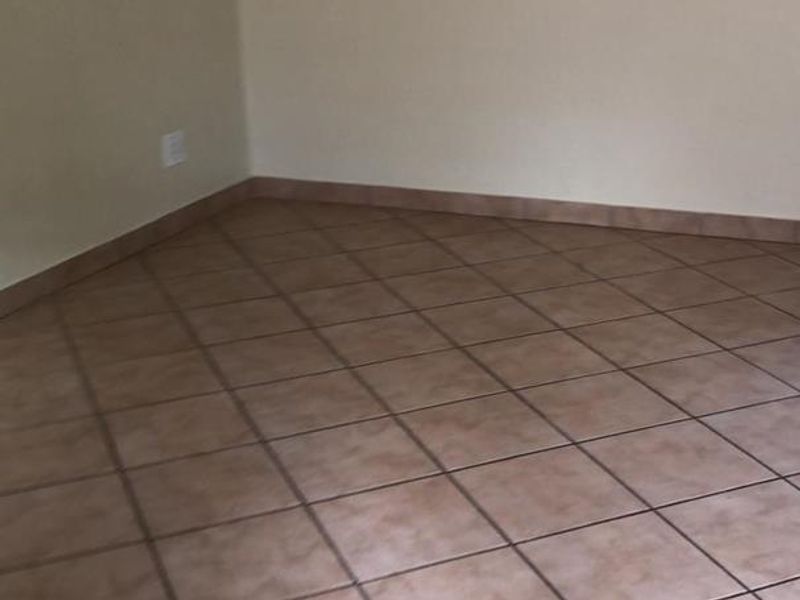 An empty living area featuring neutral wall paint and ceramic floor tiles, providing a blank canvas for interior design.