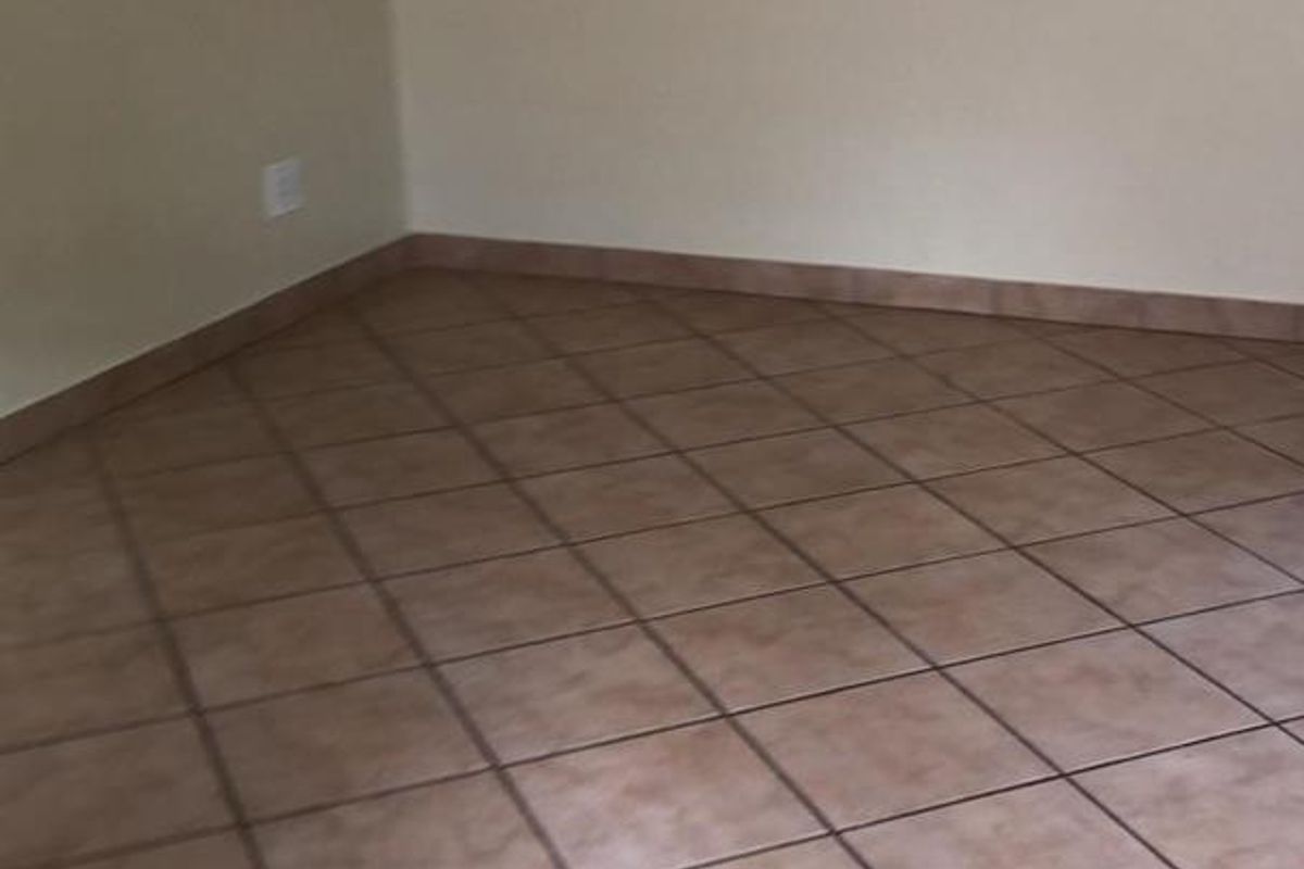An empty living area featuring neutral wall paint and ceramic floor tiles, providing a blank canvas for interior design.