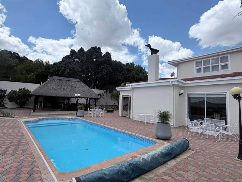Spacious outdoor pool area featuring a paved patio, swimming pool with cover, and a traditional thatched lapa for outdoor entertainment.
