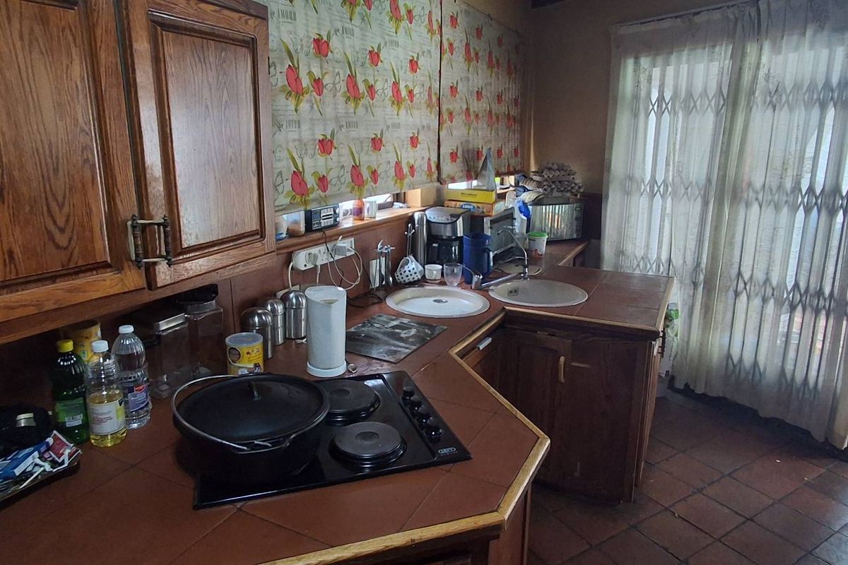 A dated kitchen featuring traditional wooden cabinetry, tiled countertops, a built-in electric hob, and direct access to an outdoor patio area.