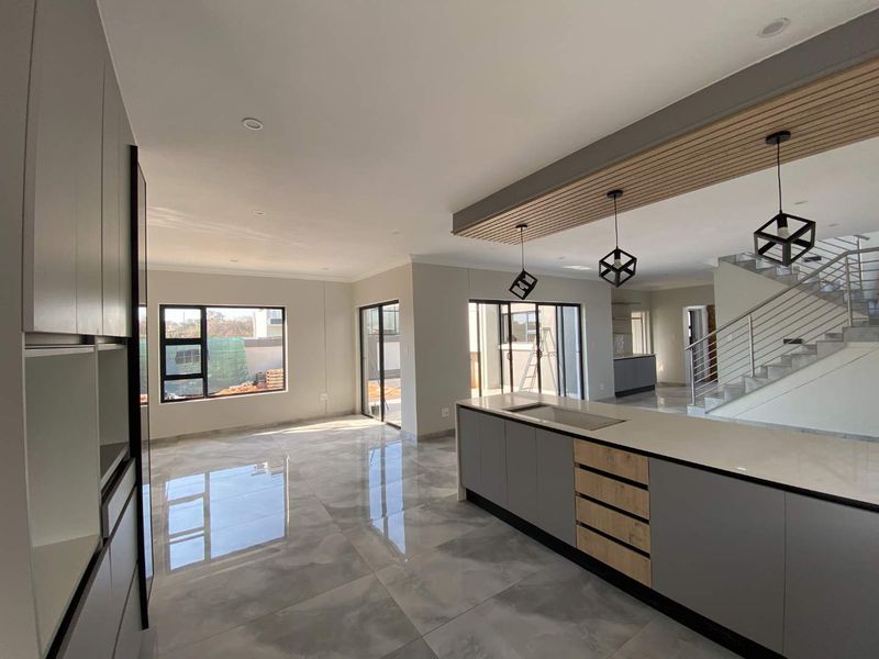Modern open-plan living area featuring a sleek kitchen island, tiled floors, and a striking slatted timber ceiling detail with contemporary pendant lighting.