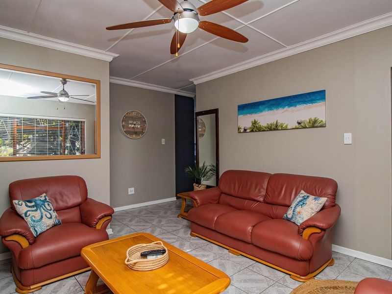 A comfortable living room featuring tiled flooring, crown molding, and a ceiling fan, with direct access to an exterior area through a security gate.