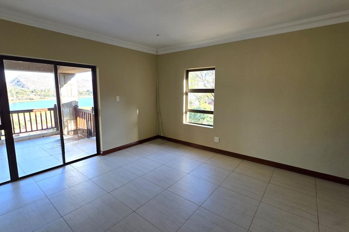 Spacious bedroom featuring neutral tiled flooring, large sliding glass doors leading to a private balcony, and scenic water views.