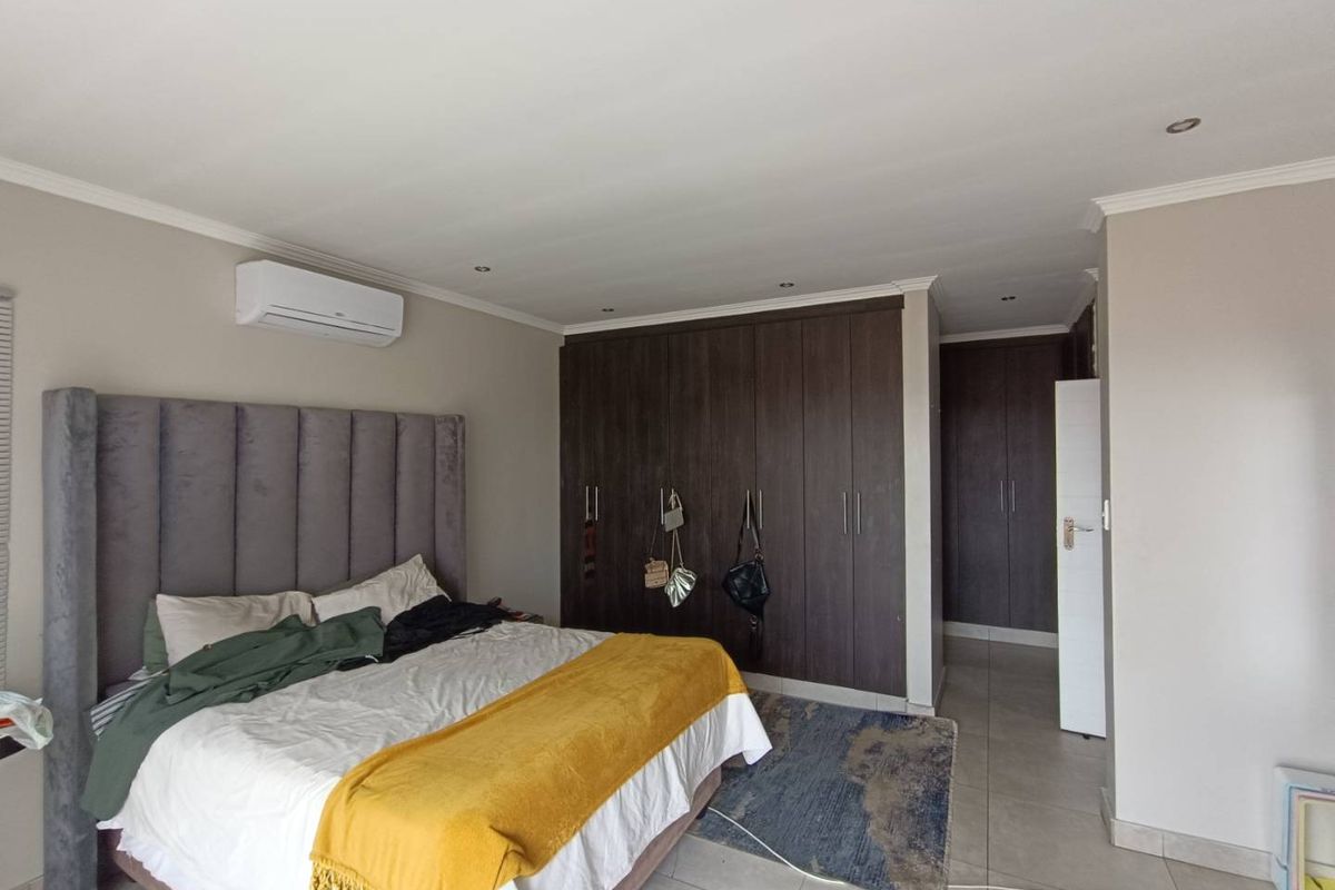 A spacious bedroom featuring built-in dark wood cabinetry, tiled flooring, recessed ceiling lighting, and a wall-mounted air conditioning unit.