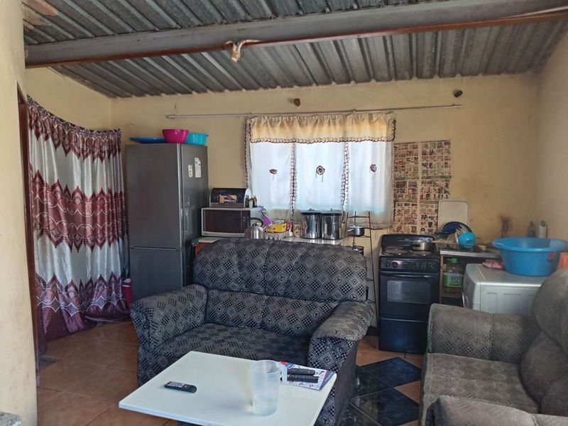 Open plan living and kitchen area featuring tiled flooring, a freestanding stove, and an exposed corrugated metal ceiling.