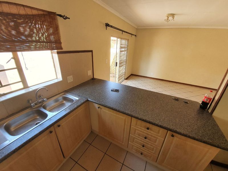 Open plan kitchen and living area featuring tiled flooring, light wood cabinetry, and a double bowl sink, with direct access to an outdoor area.
