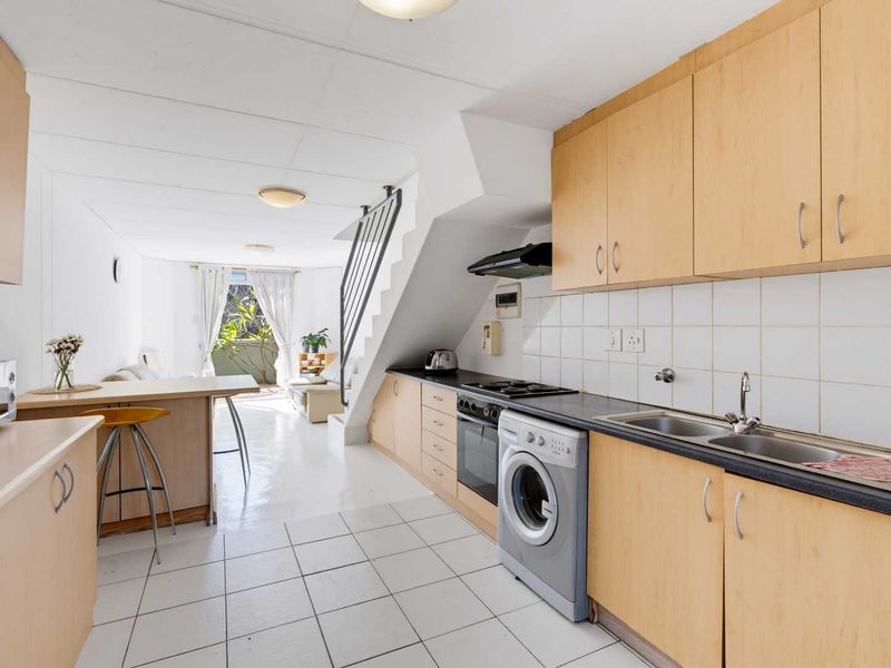 Open-plan kitchen and living area featuring light wood cabinetry, tiled flooring, and a staircase, offering a functional layout with direct access to the balcony.