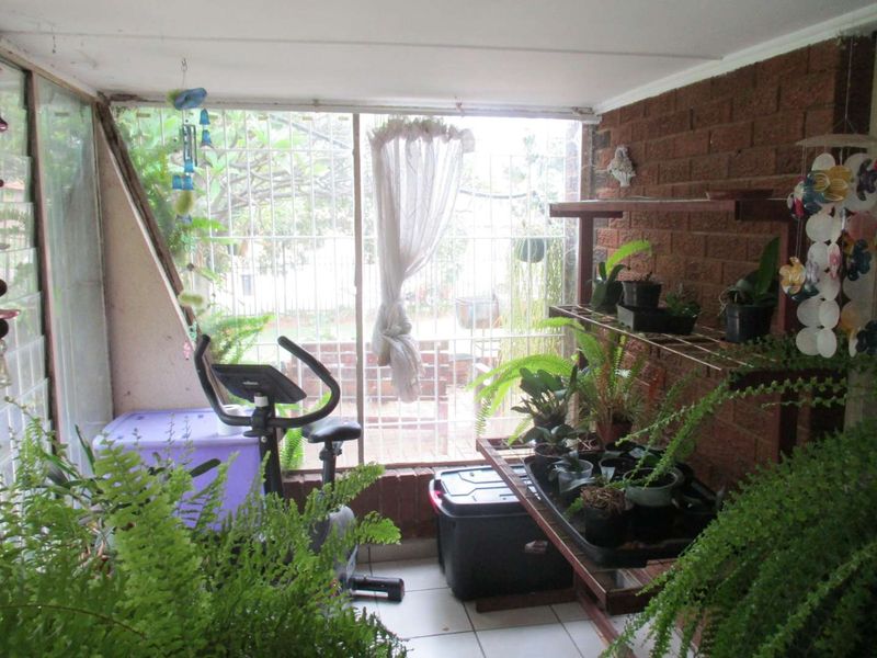 Enclosed patio area featuring exposed brick walls, tiled flooring, and security bars, offering a versatile space for relaxation or indoor gardening.