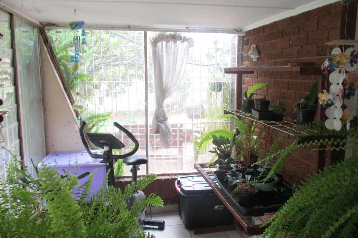 Enclosed patio area featuring exposed brick walls, tiled flooring, and security bars, offering a versatile space for relaxation or indoor gardening.