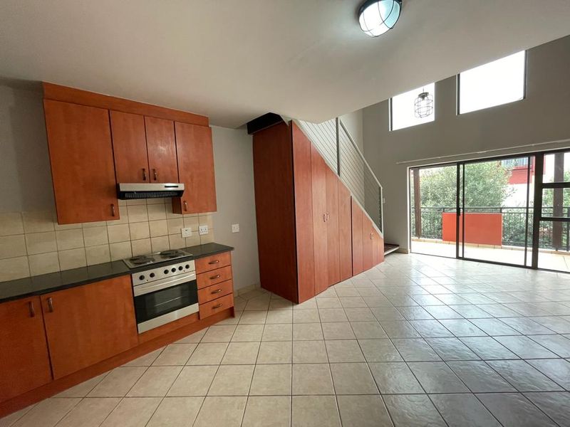 Open-plan kitchen and living area featuring wooden cabinetry, built-in appliances, tiled flooring, and direct access to a balcony through sliding glass doors.