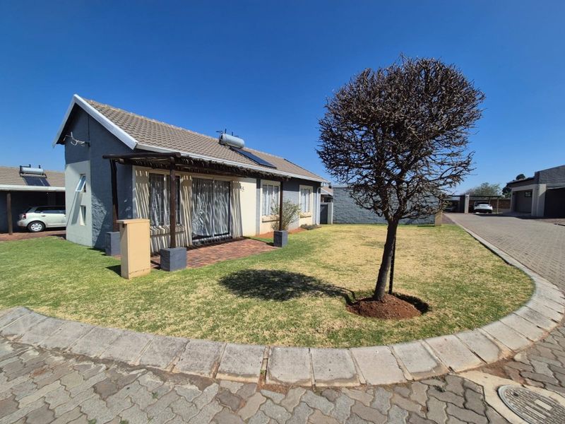 Front elevation of a townhouse featuring a tiled roof with solar water heater, a timber pergola over a paved patio, and a private garden area.