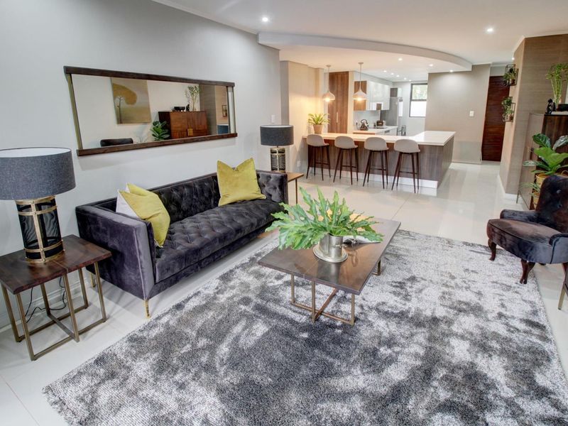 A modern open-plan living and kitchen area featuring sleek cabinetry, a central island with breakfast bar seating, and polished floor tiles throughout.