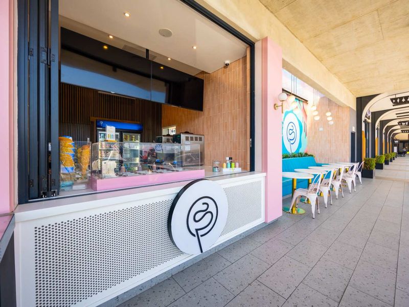 A modern commercial service kiosk featuring a bi-fold window, built-in counter, and tiled outdoor seating area under a covered walkway.