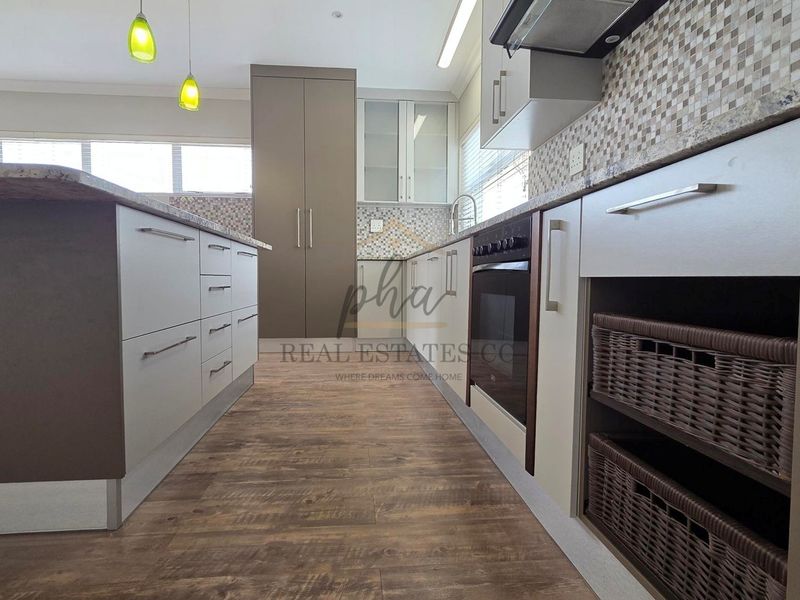 Modern kitchen featuring a central island, built-in oven, extractor fan, and stylish mosaic tile backsplash with ample cabinetry and wood-look flooring.