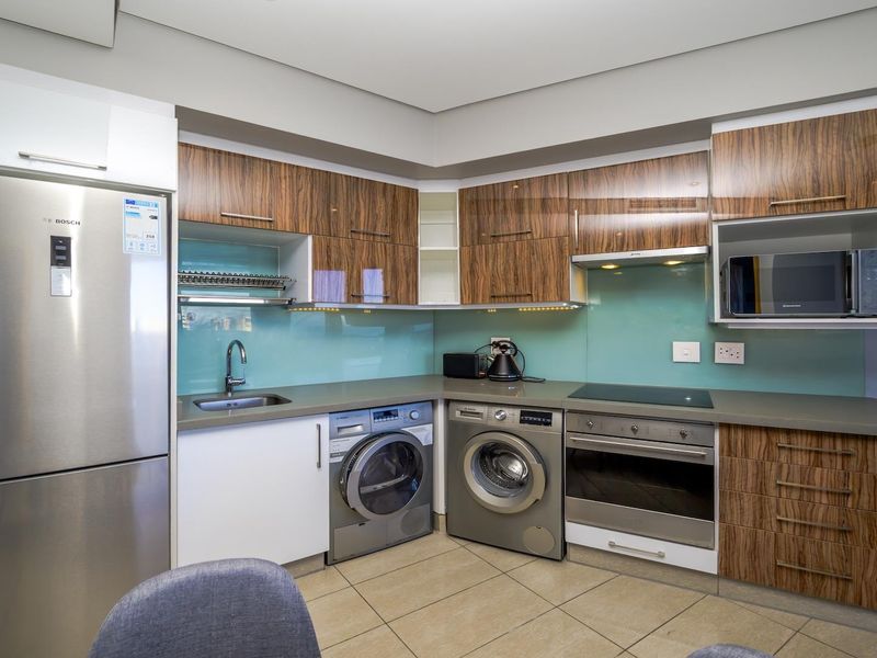 Modern kitchen featuring wood-grain cabinetry, stone countertops, glass splashback, and integrated stainless steel appliances including an oven, cooktop, and microwave.
