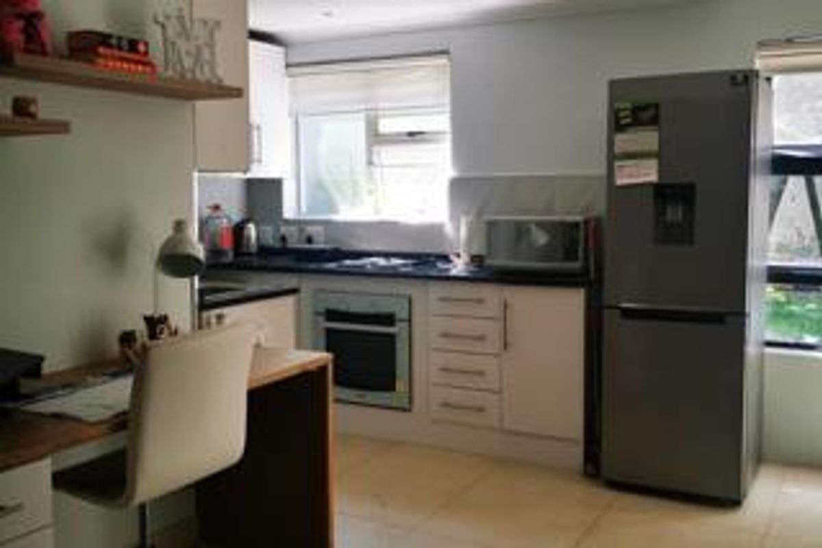 A functional kitchen featuring built-in cabinetry, an integrated oven and hob, tiled flooring, and a window providing natural light.
