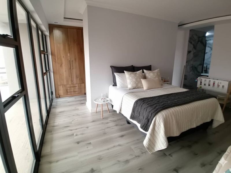 Modern bedroom featuring light laminate flooring, built-in wooden wardrobe, and large aluminium sliding doors providing ample natural light.