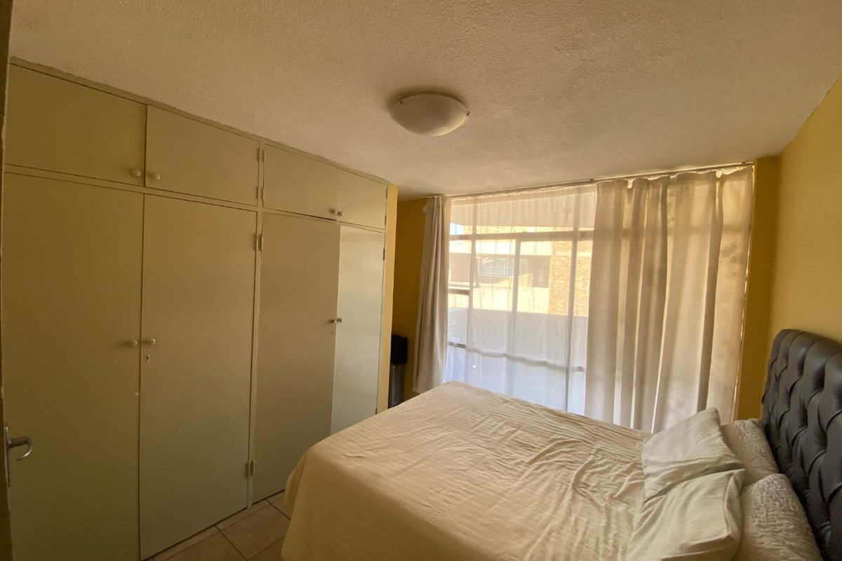 A bedroom featuring built-in floor-to-ceiling cupboards, tiled flooring, and large windows allowing natural light, providing a functional and practical living space.