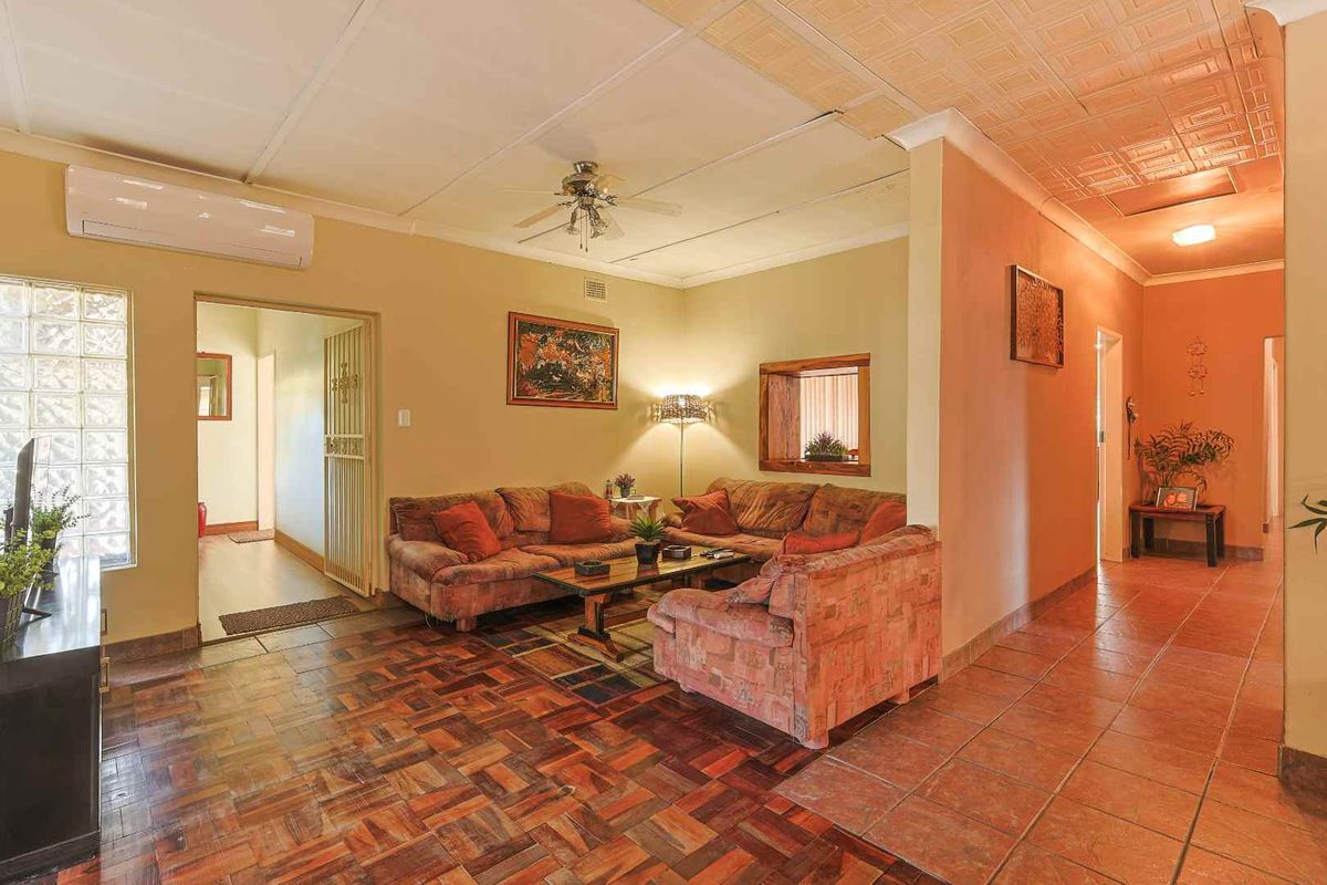 Spacious living area featuring parquet flooring, a ceiling fan, wall-mounted air conditioning unit, and glass block window detailing.