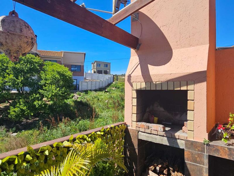 Outdoor patio area featuring a built-in brick braai, timber pergola structure, and tiled prep surface, overlooking a natural garden setting.