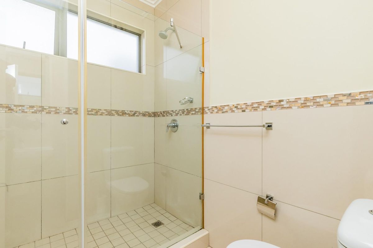 A clean, modern bathroom featuring a glass-enclosed shower, neutral wall tiles with a decorative mosaic border, and standard white sanitary ware.