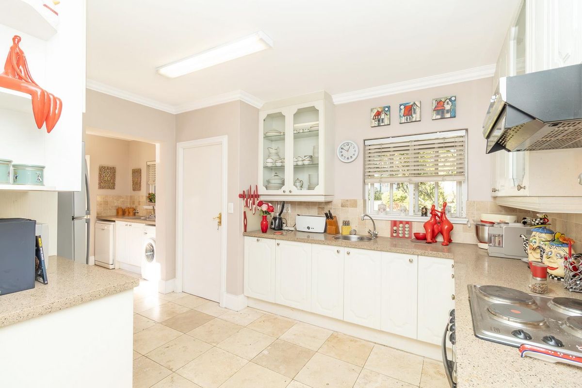 A functional kitchen featuring white cabinetry, stone-look countertops, tiled flooring, and an integrated hob and extractor fan, with an adjacent scullery area.